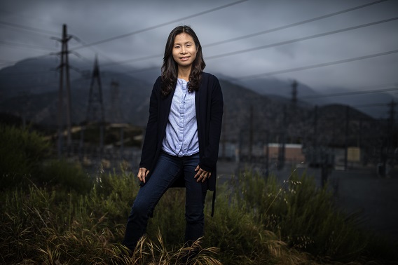 A woman standing at a hill with distribution wires in the background facing the camera