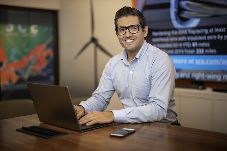 Man with glasses smiling at camera with a laptop