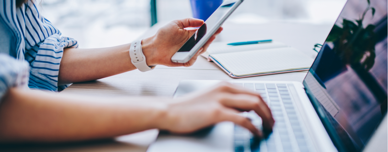 A picture of someone grabbing a phone with one hand and touching a laptop's keyboard with their other hand