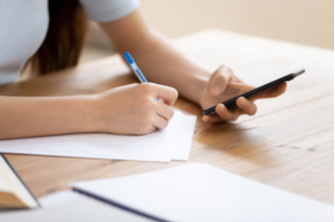 A person grabbing a phone with one hand and writing something with their other hand