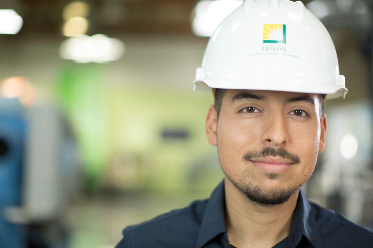 A young man wearing a hard hat smiling at the camera