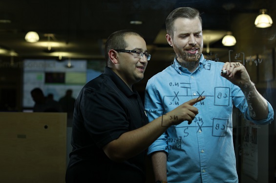 Two men writing on a clear board