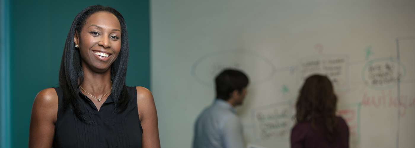 A smiling woman with people back writing on a board in the background