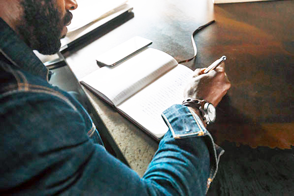 A man with a pen in hand writing in a notebook