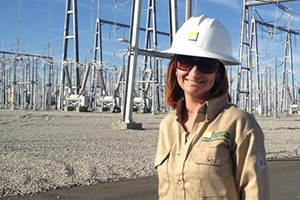A woman standing in front of a grid with a hard hat smiling.