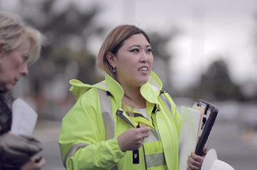 A woman wearing a yellow protective jacket holding folders and looking toward the right