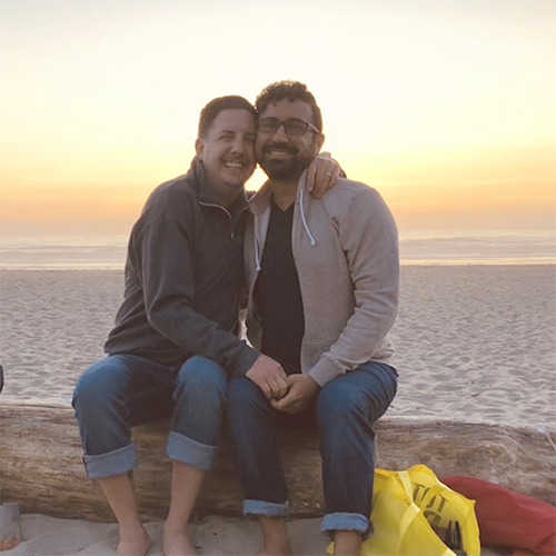 2 men sitting down on the beach smiling