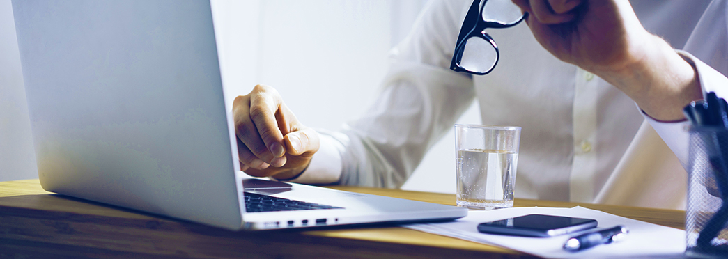 Torso of a man sitting in workspace set up with computer, a glass of water and other gadgets