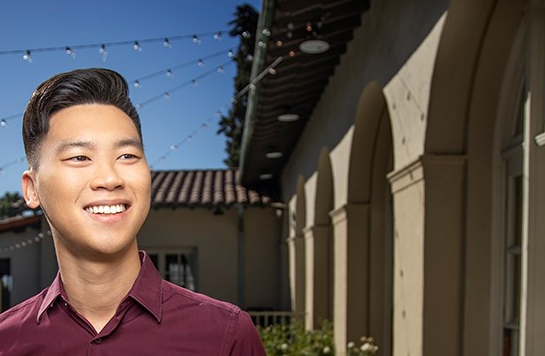 A man in front of a building smiling away from the camera
