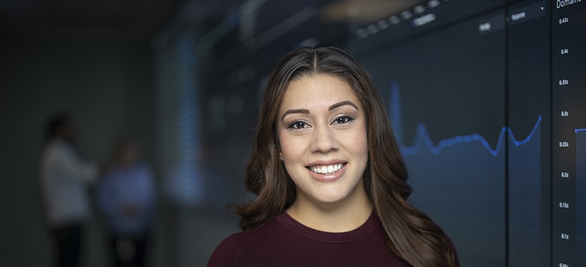 A woman looking at the camera with a monitor in the background